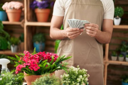 Téléchargez les photos : Jeune homme latin fleuriste comptant les dollars à la boutique de fleurs - en image libre de droit