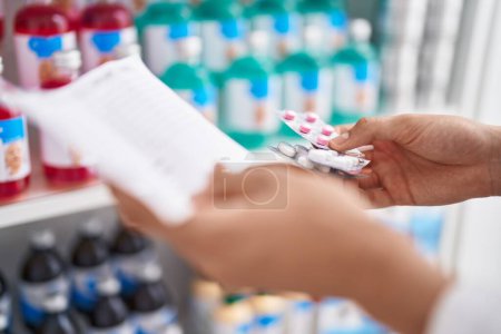 Téléchargez les photos : Jeune homme blond pharmacien tenant des pilules et du papier sur ordonnance à la pharmacie - en image libre de droit