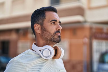 Téléchargez les photos : Jeune homme hispanique portant des écouteurs avec une expression détendue dans la rue - en image libre de droit