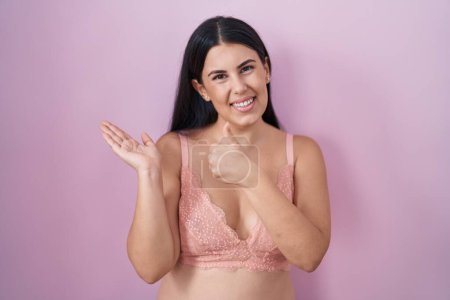 Photo for Young hispanic woman wearing pink bra showing palm hand and doing ok gesture with thumbs up, smiling happy and cheerful - Royalty Free Image