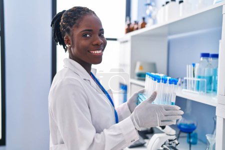 Téléchargez les photos : African american woman wearing scientist uniform holding test tubes at laboratory - en image libre de droit