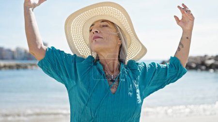 Téléchargez les photos : Femme aux cheveux gris d'âge moyen respirant les bras ouverts à la plage - en image libre de droit