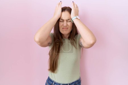 Photo for Beautiful brunette woman standing over pink background suffering from headache desperate and stressed because pain and migraine. hands on head. - Royalty Free Image
