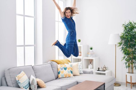 Foto de Mujer joven sonriendo confiado saltando en el sofá en casa - Imagen libre de derechos