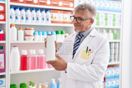 Photo for Middle age grey-haired man pharmacist holding shampoo bottle at laboratory - Royalty Free Image