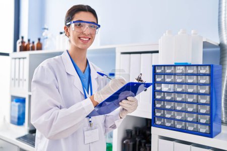 Photo for Young beautiful hispanic woman scientist writing report working at laboratory - Royalty Free Image
