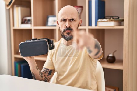 Téléchargez les photos : Jeune homme hispanique portant des lunettes de réalité virtuelle pointant du doigt vers la caméra et vers vous, geste confiant et sérieux - en image libre de droit