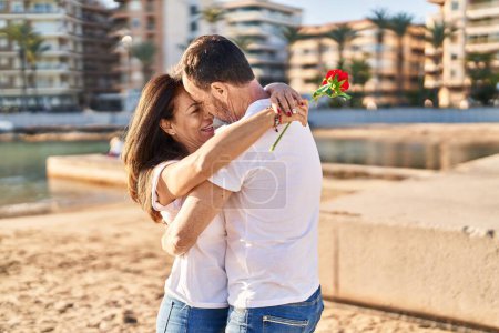 Téléchargez les photos : Moyen âge homme et femme couple étreignant l'autre surprise avec des fleurs au bord de la mer - en image libre de droit