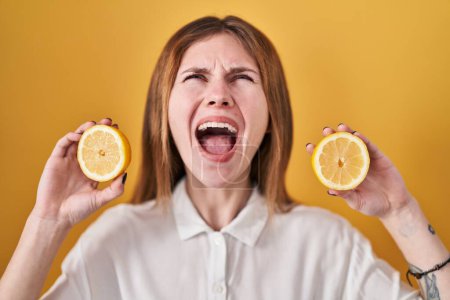 Photo for Beautiful woman holding lemons angry and mad screaming frustrated and furious, shouting with anger looking up. - Royalty Free Image