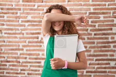 Photo for Young caucasian woman holding art notebook smiling cheerful playing peek a boo with hands showing face. surprised and exited - Royalty Free Image