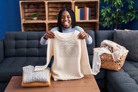 Photo for African american woman folding clean laundry sticking tongue out happy with funny expression. - Royalty Free Image