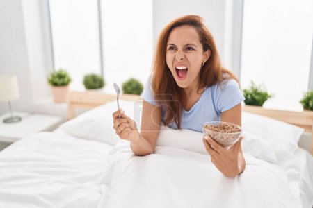 Foto de Mujer morena desayunando en la cama enojada y loca gritando frustrada y furiosa, gritando de rabia. rabia y concepto agresivo. - Imagen libre de derechos