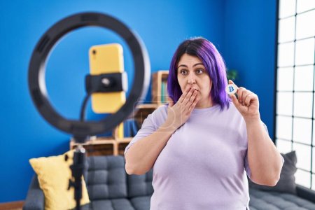 Foto de Además tamaño mujer ingenio púrpura grabación de pelo bitcoin tutorial con teléfono inteligente en casa cubriendo la boca con la mano, sorprendido y miedo de error. expresión sorprendida - Imagen libre de derechos