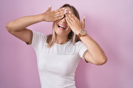 Photo for Blonde caucasian woman standing over pink background covering eyes with hands smiling cheerful and funny. blind concept. - Royalty Free Image