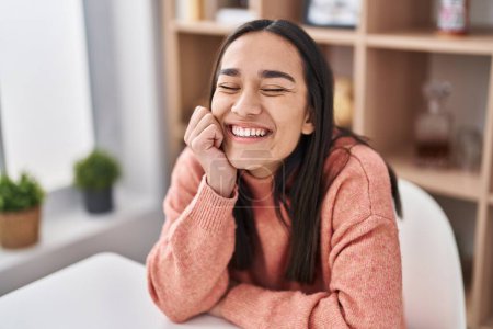 Téléchargez les photos : Jeune femme hispanique souriant confiant assis sur la table à la maison - en image libre de droit