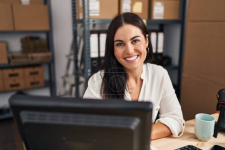 Téléchargez les photos : Jeune belle hispanique femme commerce électronique travailleur d'affaires souriant confiant assis sur la table au bureau - en image libre de droit