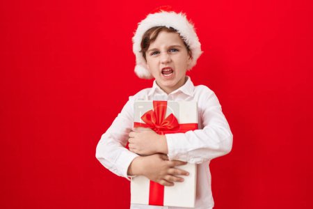 Photo for Little caucasian boy wearing christmas hat and holding gifts clueless and confused expression. doubt concept. - Royalty Free Image