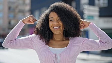 Foto de Mujer afroamericana sonriendo confiada haciendo un gesto fuerte con los brazos en la calle - Imagen libre de derechos