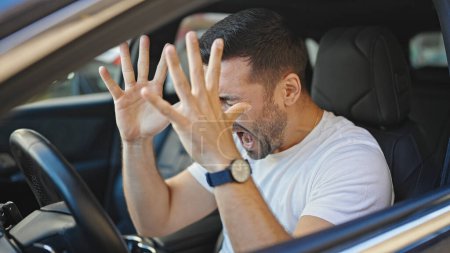 Foto de Joven hispano estresado conduciendo coche gritando en la calle - Imagen libre de derechos