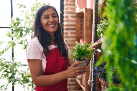 Photo for Young beautiful hispanic woman florist holding plant at flower shop - Royalty Free Image