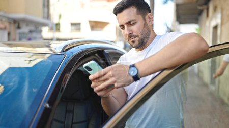 Téléchargez les photos : Young hispanic man using smartphone leaning on car at street - en image libre de droit