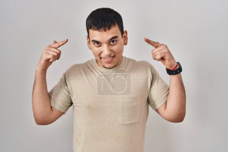 Foto de Hombre árabe joven vistiendo camiseta casual sonriendo apuntando a la cabeza con ambas manos dedo, gran idea o pensamiento, buena memoria - Imagen libre de derechos