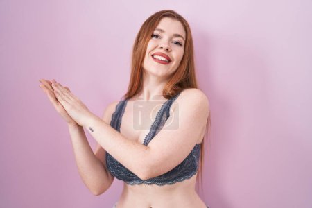 Photo for Redhead woman wearing lingerie over pink background clapping and applauding happy and joyful, smiling proud hands together - Royalty Free Image