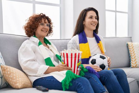 Téléchargez les photos : Mère et fille hispaniques regardant le football soutenir l'équipe regardant positif et heureux debout et souriant avec un sourire confiant montrant les dents - en image libre de droit