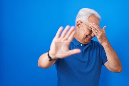 Photo for Middle age man with grey hair standing over blue background covering eyes with hands and doing stop gesture with sad and fear expression. embarrassed and negative concept. - Royalty Free Image