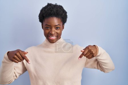 Foto de Mujer afroamericana de pie sobre fondo azul mirando confiado con sonrisa en la cara, señalándose con los dedos orgullosos y felices. - Imagen libre de derechos