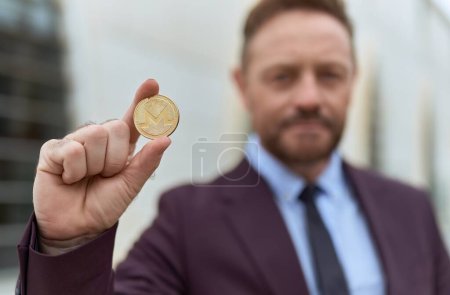 Middle age man business worker holding monero crypto currency at street