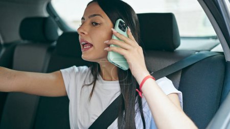 Photo for Young beautiful hispanic woman passenger talking on smartphone telling destination to taxi driver at street - Royalty Free Image