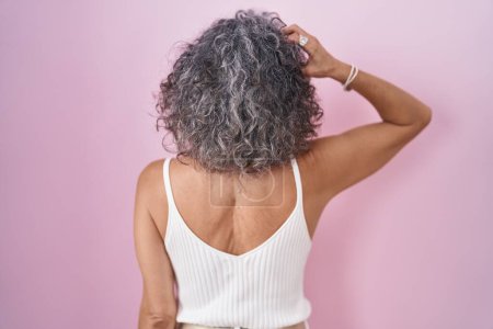 Foto de Mujer de mediana edad con el pelo gris de pie sobre fondo rosa hacia atrás pensando en la duda con la mano en la cabeza - Imagen libre de derechos