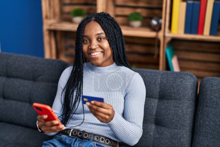 Photo for African american woman using smartphone and credit card sitting on sofa at home - Royalty Free Image