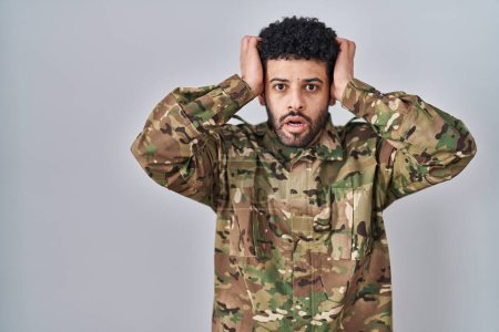 Téléchargez les photos : Arabe homme portant camouflage uniforme de l'armée fou et effrayé avec les mains sur la tête, peur et surpris de choc avec la bouche ouverte - en image libre de droit