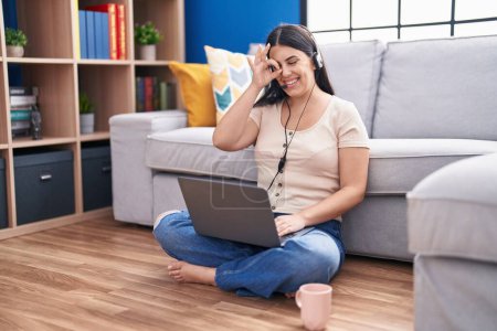 Photo for Young hispanic woman using laptop at home smiling happy doing ok sign with hand on eye looking through fingers - Royalty Free Image