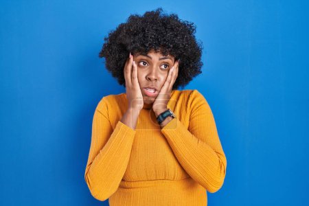 Téléchargez les photos : Femme noire avec les cheveux bouclés debout sur fond bleu mains fatiguées couvrant le visage, la dépression et la tristesse, bouleversé et irrité par le problème - en image libre de droit