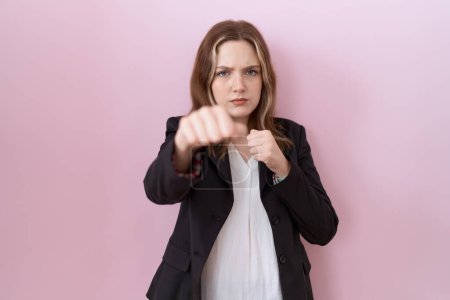Téléchargez les photos : Jeune femme d'affaires caucasienne portant une veste noire poing poing pour se battre, attaque agressive et en colère, menace et violence - en image libre de droit