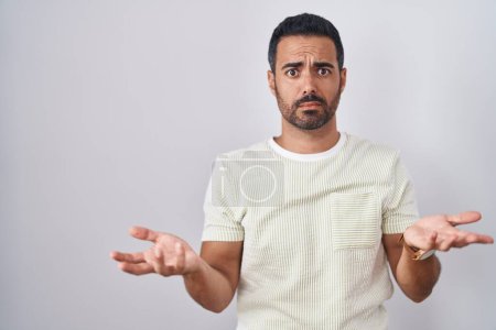 Photo for Hispanic man with beard standing over isolated background clueless and confused with open arms, no idea concept. - Royalty Free Image