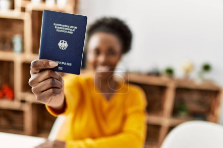 Téléchargez les photos : African american woman holding deutchland passport sitting on table at home - en image libre de droit