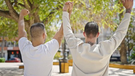 Téléchargez les photos : Deux hommes couple avec les mains levées ensemble au parc - en image libre de droit