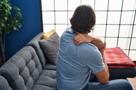 Téléchargez les photos : Homme d'âge moyen souffrant de maux de dos assis sur le canapé à la maison - en image libre de droit