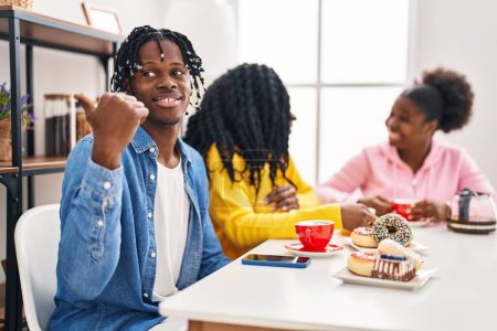 Photo for Group of three young black people sitting on a table having coffee pointing thumb up to the side smiling happy with open mouth - Royalty Free Image