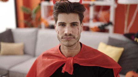 Foto de Joven hombre hispano con traje de diablo teniendo fiesta de halloween en casa - Imagen libre de derechos