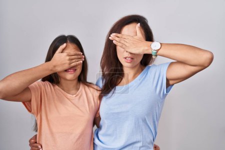 Photo for Young mother and daughter standing over white background covering eyes with hand, looking serious and sad. sightless, hiding and rejection concept - Royalty Free Image