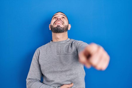 Téléchargez les photos : Homme hispanique debout sur fond bleu se moquant de vous, pointant du doigt la caméra avec la main sur le corps, expression de honte - en image libre de droit