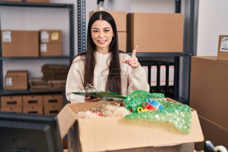 Photo for Young woman working at small business ecommerce smiling happy pointing with hand and finger to the side - Royalty Free Image
