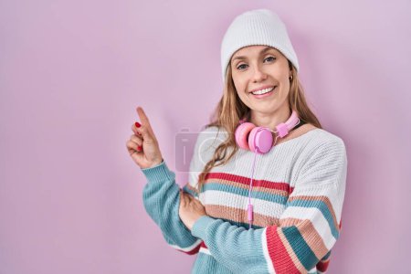 Téléchargez les photos : Jeune femme blonde debout sur fond rose avec un grand sourire sur le visage, pointant avec la main et le doigt vers le côté en regardant la caméra. - en image libre de droit