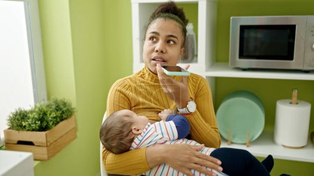 Téléchargez les photos : Mère et fils envoient un message vocal par téléphone intelligent allaitant bébé à la salle à manger - en image libre de droit