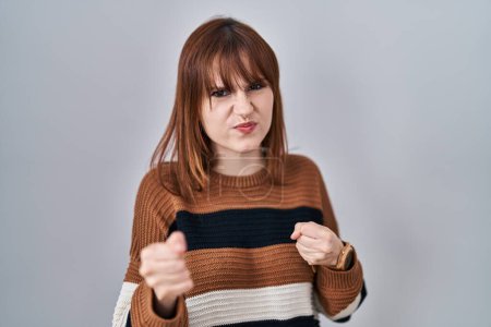 Foto de Mujer hermosa joven con suéter a rayas sobre fondo aislado listo para luchar con el gesto de defensa del puño, cara enojada y molesta, miedo al problema - Imagen libre de derechos